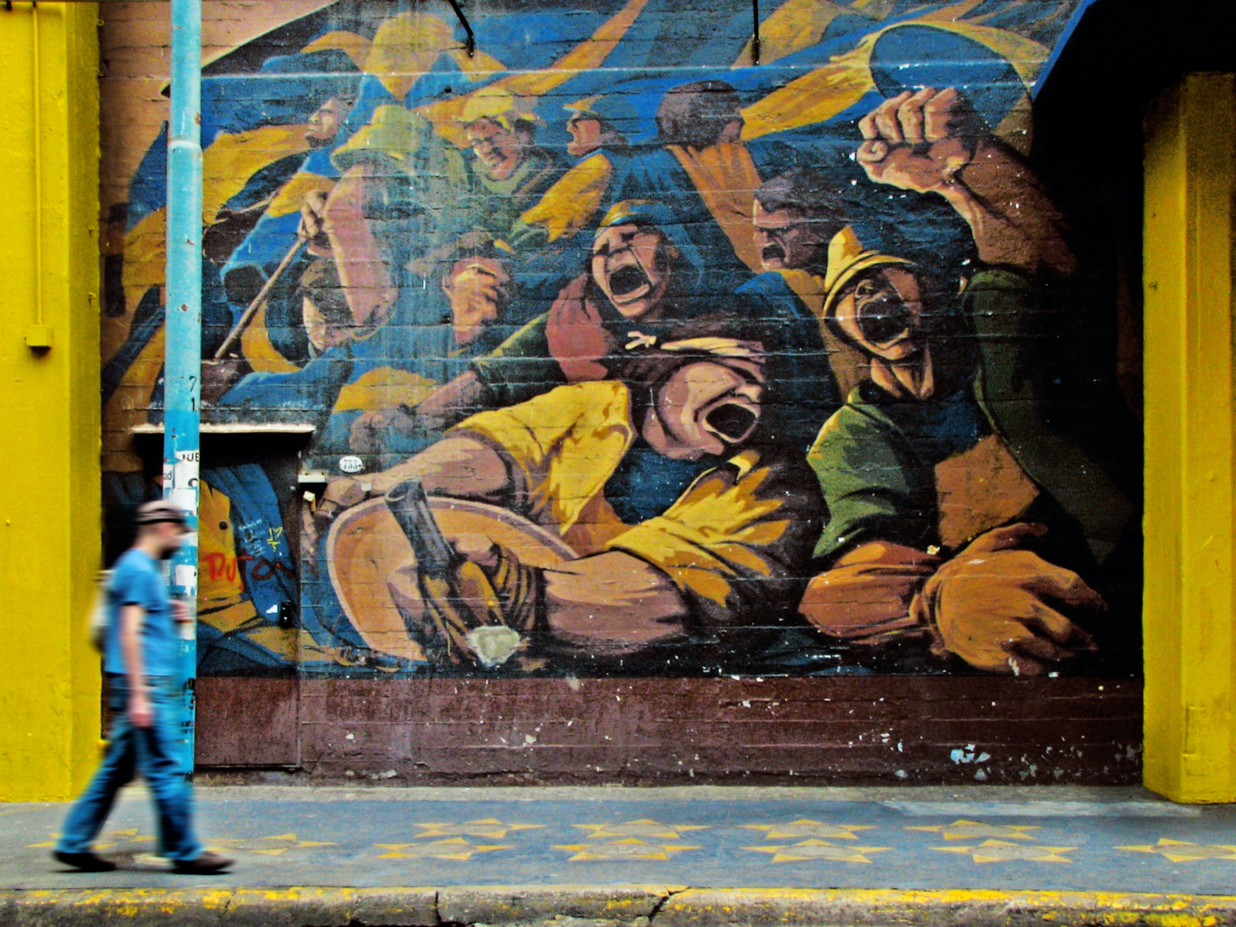 Man walking by a street mural depicting workers