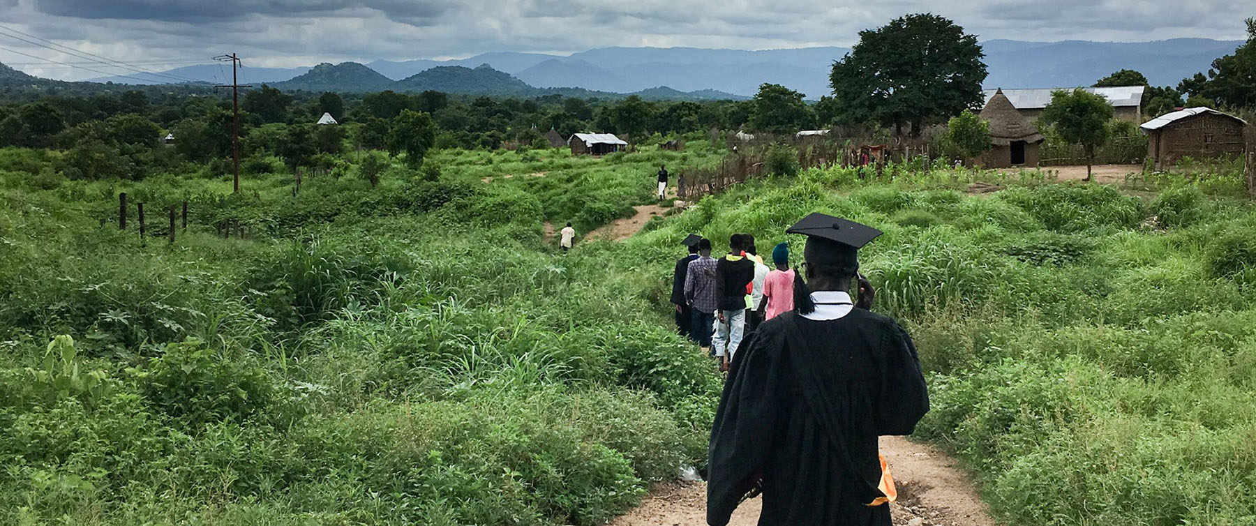 Student with a graduation cap walking in along a path in a lush green field